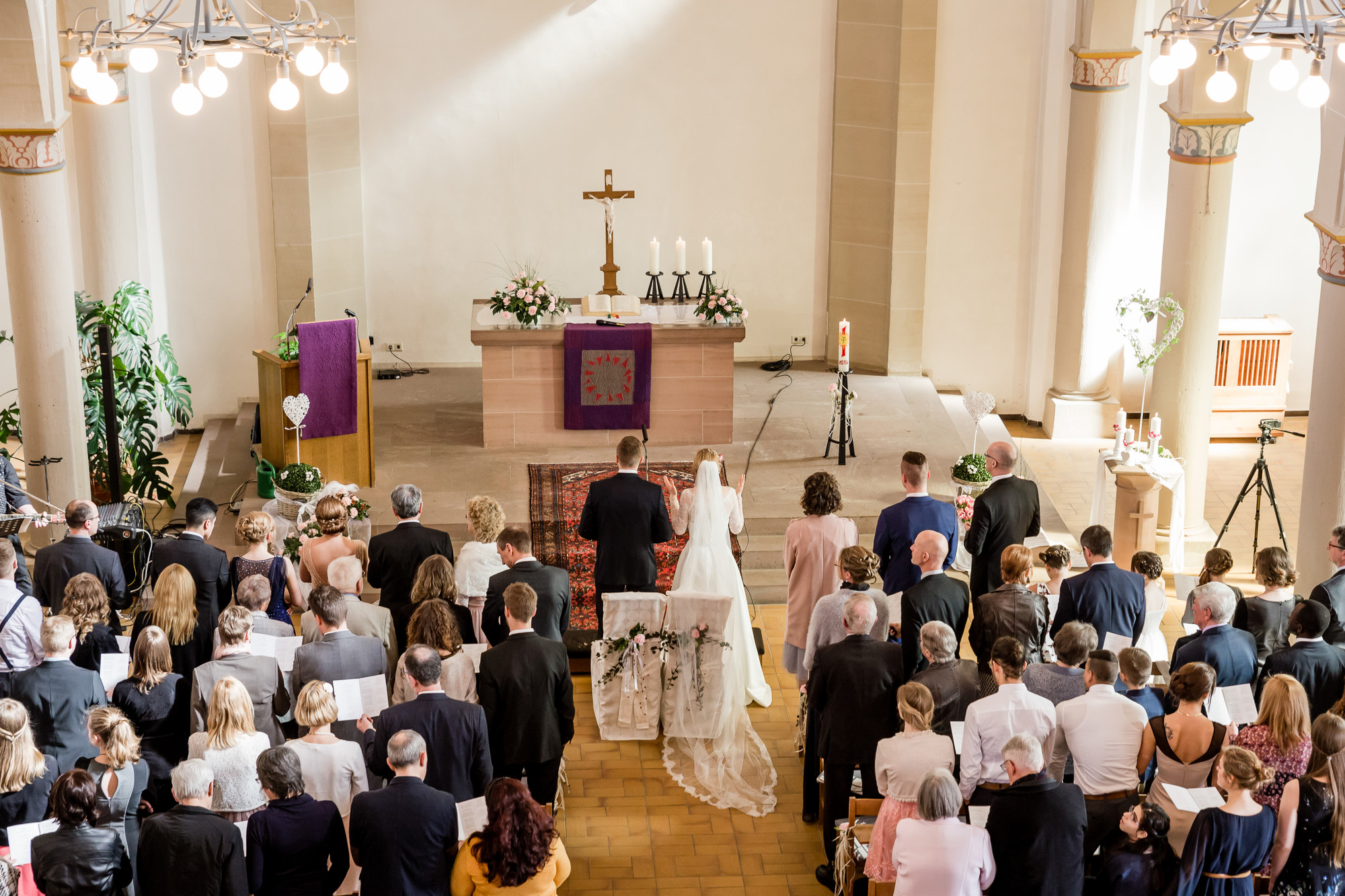 Das Brautpaar und die Gäste der Zeremonie stehen im festlich geschmückten Kirchensaal.