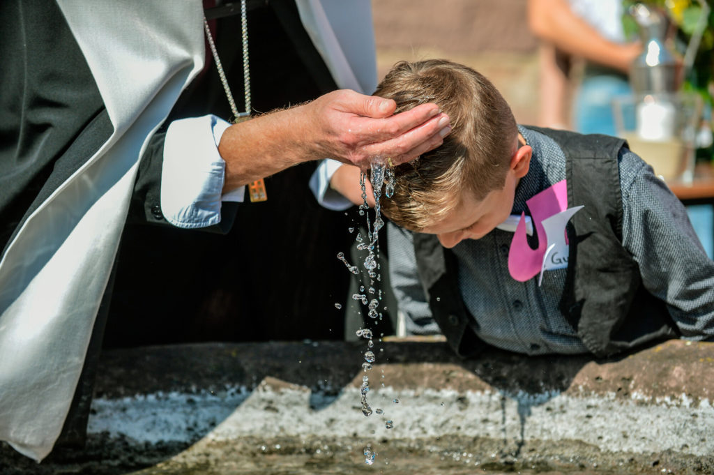 Junge wie er gerade das Taufwasser über seinen Kopf gegossen bekommt.